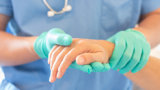 Médica com luvas verdes segura mão de paciente no hospital.